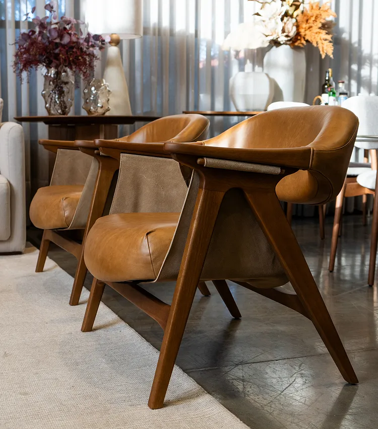 Par de poltronas de couro marrom com estrutura em madeira em ambiente decorado.